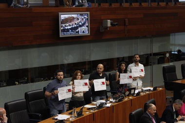 Diputados de Podemos muestran en el pleno de la Asamblea un cartel de apoyo a los procesados por irrumpir en TVE